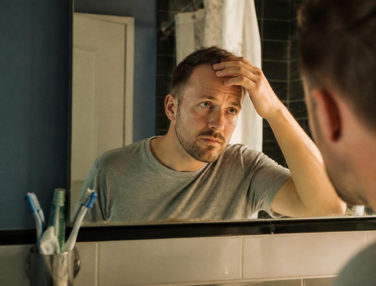 Man checking his hairline in a bathroom mirror